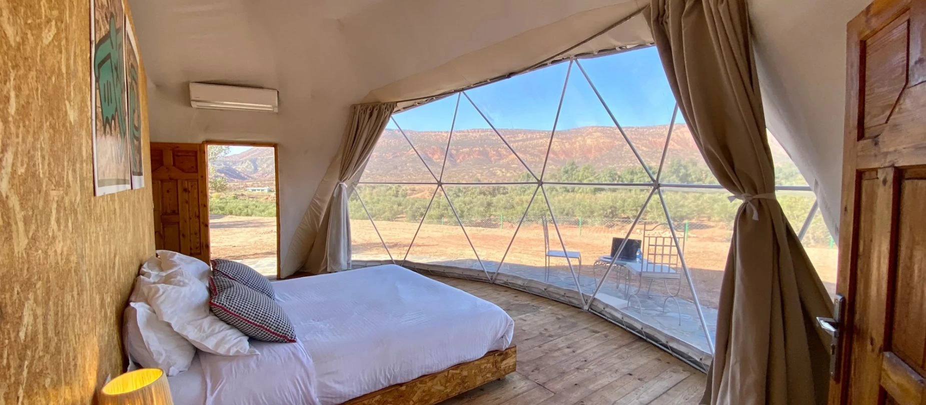 Interieur d'un dome avec lit face a une large baie geodesique ouverte sur les collines arides de Ouirgane